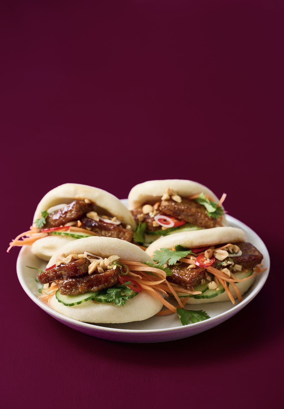 Steamed bao buns filled with marinated Millow strips on a deep aubergine background