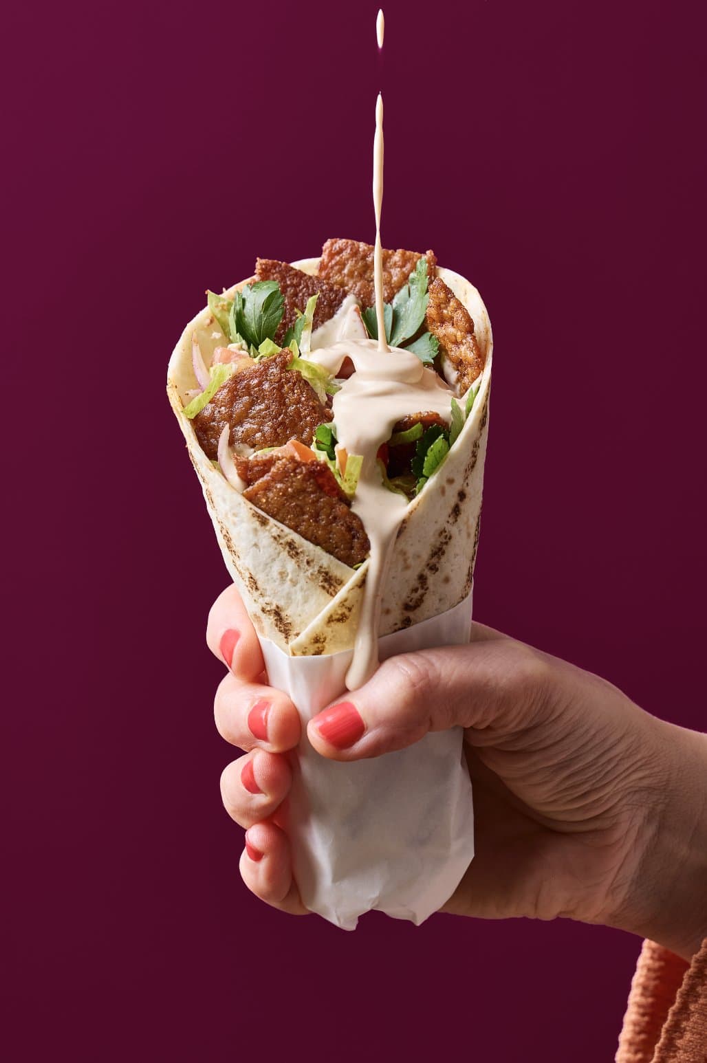 A hand holding a kebab wrap filled with seared Millow slices